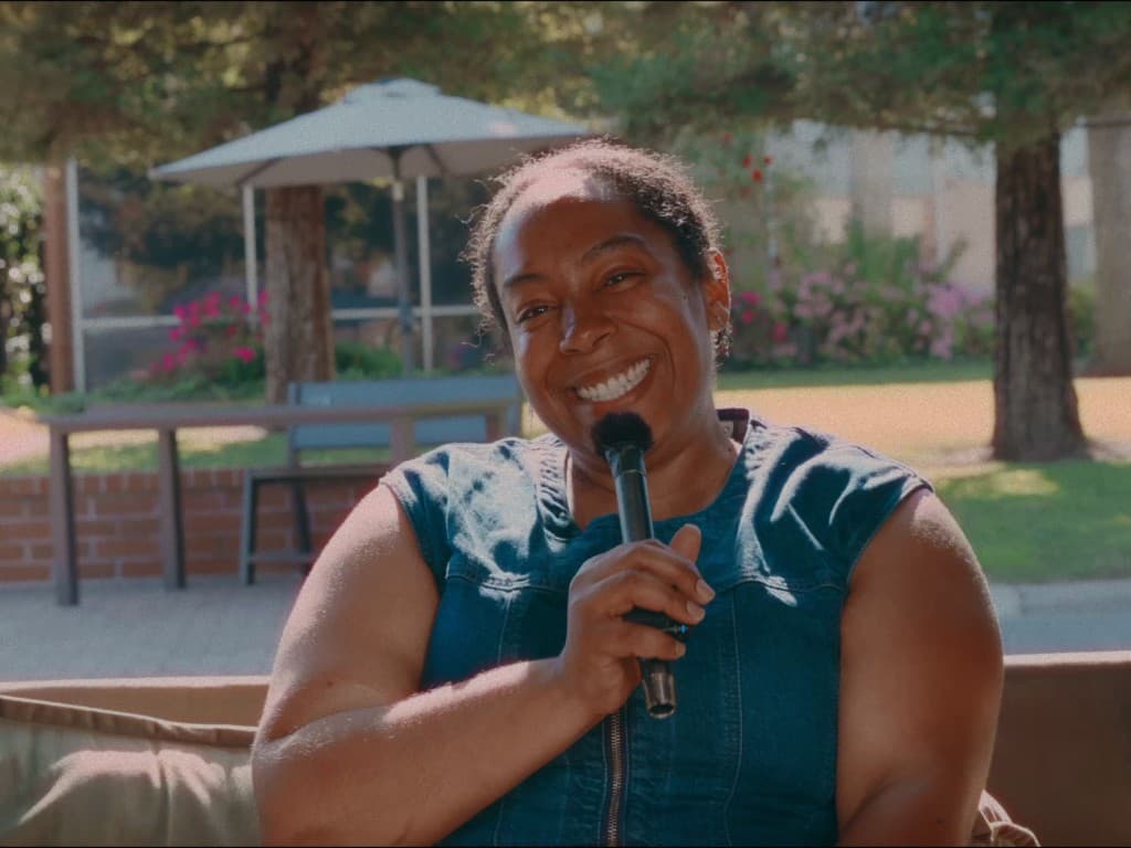 Person smiling while holding a microphone in a warm outdoor setting